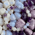 Bracelet Bien-être Ménopause LORRAHA posé sur des pierres roulées violettes, bleu pâle et blanches