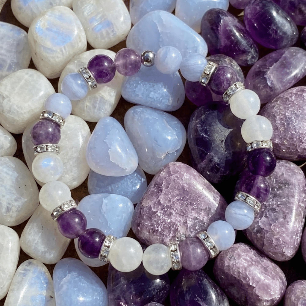 Bracelet Bien-être Ménopause LORRAHA posé sur des pierres roulées violettes, bleu pâle et blanches